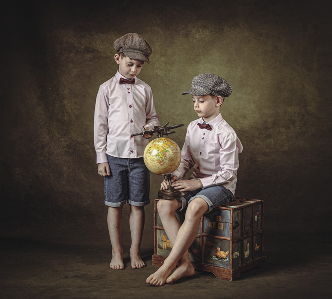 Two young boys in an old style fine art portrait looking at a globe of the world, Limerick. Ireland.  